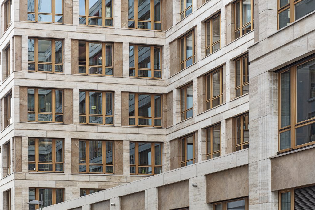 Eckansicht eines modernen Gebäudes mit beigefarbener Natursteinfassade und großen Holzrahmenfenstern.