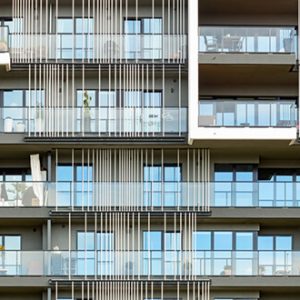 Nahaufnahme der modernen Fassade eines Wohngebäudes mit bodentiefen Fenstern und durchgehenden Balkonen, die durch vertikale Metallstreben akzentuiert sind. Die Balkone zeigen persönliche Details wie Möbel und Pflanzen.