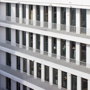 Detailaufnahme einer modernen Fassade mit weißen Balkongeländern, großen Fenstern und klaren Linien.