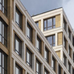 Nahaufnahme eines modernen Bürogebäudes mit einer Fassade aus weißen Steinrahmen, beigefarbenen Akzenten und großen Glasfenstern.