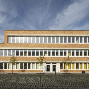 Backsteingebäude mit weißen Fenstern und einem Innenhof mit kleinen Bäumen.