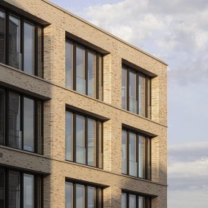 Detailaufnahme einer modernen Fassade aus hellen Ziegelsteinen mit großen, bodentiefen Fenstern, die durch schmale Rahmen eingefasst sind.